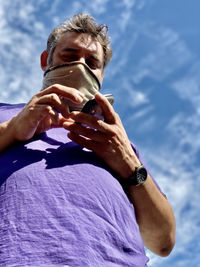 Portrait of man holding iphone against sky