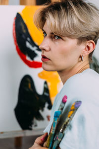 Creative portrait of beautiful young woman artist in studio with brushes.