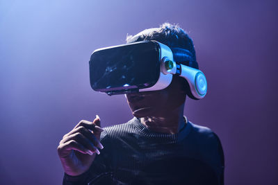 Astonished female african american gamer in modern vr goggles standing on dark background in studio while experiencing virtual reality in neon illumination