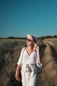 Young woman wearing sunglasses standing on field against clear sky
