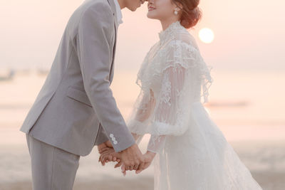 Midsection of bride and bridegroom holding hands at beach