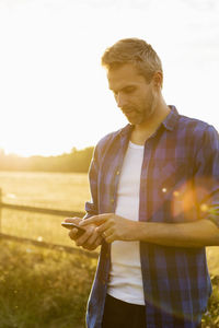 Man using phone while standing on field against sky