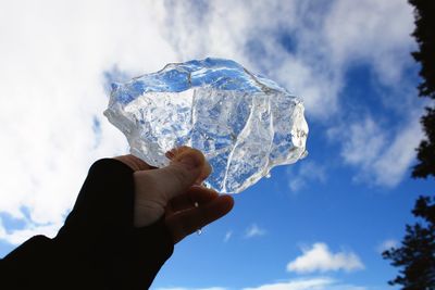 Low angle view of hand holding ice against sky