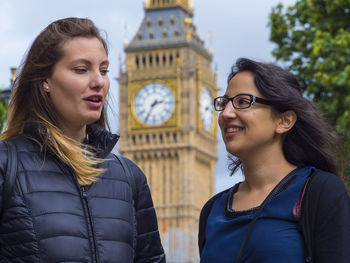 Smiling female friends talking while standing in city