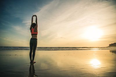 Rear view of woman exercising on shore at beach