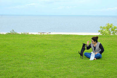 Friends sitting on grass by sea against sky
