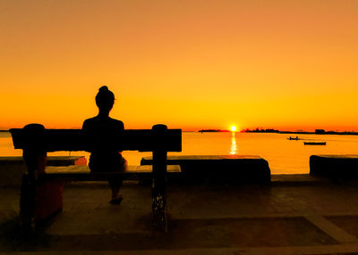 Silhouette man sitting on bench by sea against sky during sunset