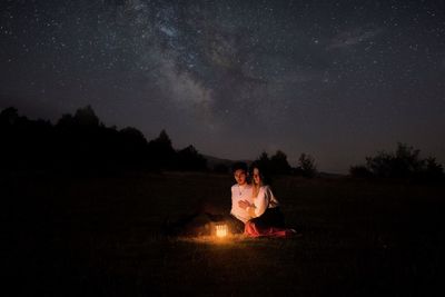People sitting on field against sky at night