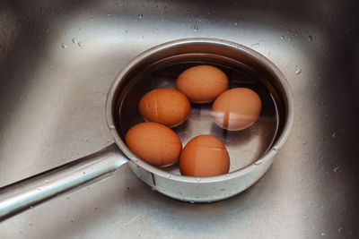 Boiled chicken eggs lie in a ladle with cold water