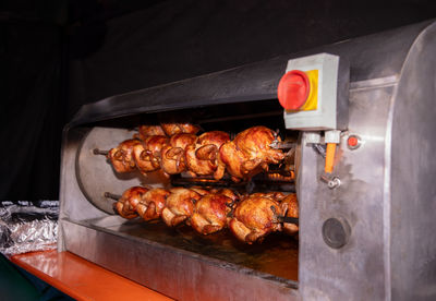 Multiple chickens on a rotisserie spit, cooking with flames in an industrial machine, golden brown