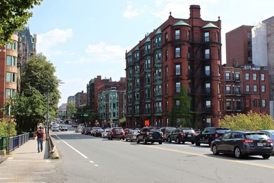 Cars on road by buildings in city against sky