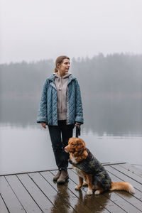 Young woman looking away while standing on pier against lake