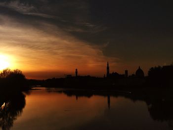 Scenic view of river by silhouette buildings against sky during sunset