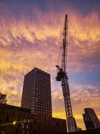 Low angle view of crane and buildings against sky during sunset