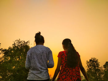 Rear view of friend standing against orange sky