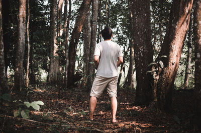 Rear view of man standing by trees in forest