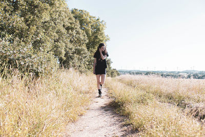 Full length of woman walking on footpath amidst field