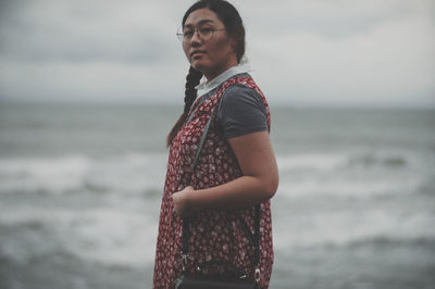 Young woman standing on beach against sky