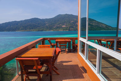 Empty chairs and table by sea against sky