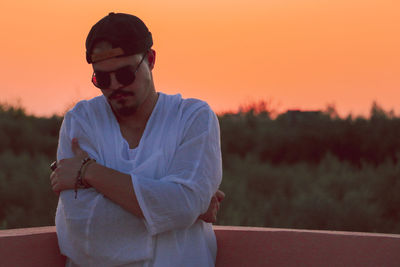 Young man wearing sunglasses standing against sky during sunset