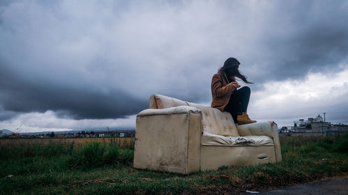 Man sitting on field against sky