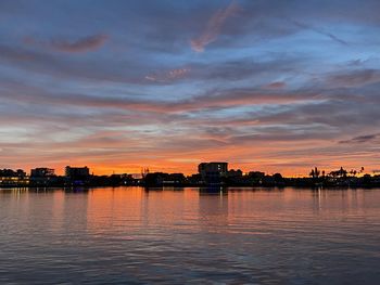 Scenic view of river by buildings against sky during sunset