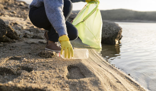 Woman picking up plastic bottle on beach by seashore