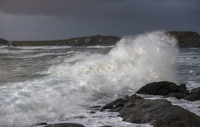 Waves splashing on rocks against sky