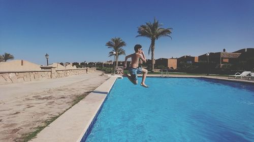 Boy jumping in swimming pool against clear blue sky