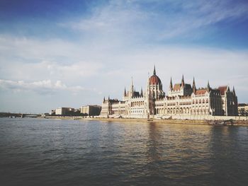 View of buildings by river against cloudy sky