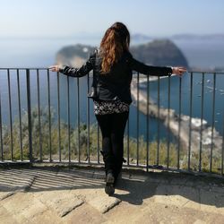 Rear view of woman standing on railing against sea