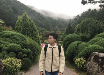 Man looking away while standing on footpath against trees