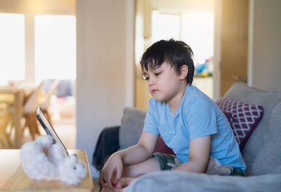 Boy looking away while sitting on bed at home