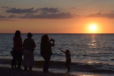 People standing on beach against sky during sunset