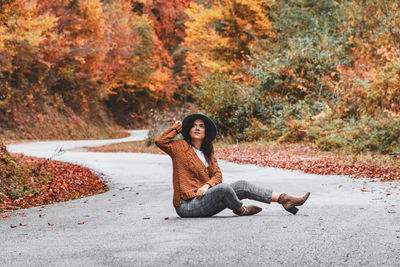 Young woman in autumn clothes sitting in the middle of road. fall colors, style.