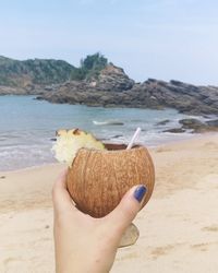 Cropped hand of woman holding drink in coconut shell against sea