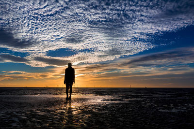 Silhouette man standing at beach against sky during sunset