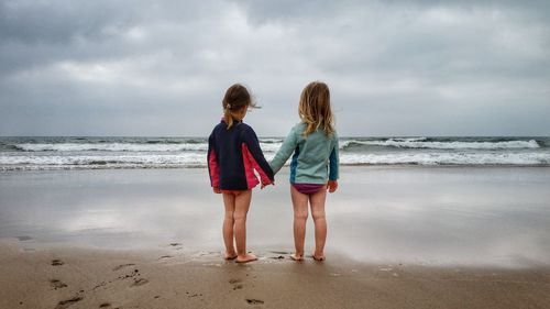 Rear view of girls on beach against sky
