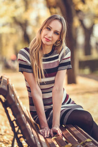 Portrait of young woman sitting on bench at park during autumn