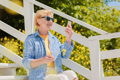 Mature woman sitting alone on the terrace of beach cafe and using mobile phone