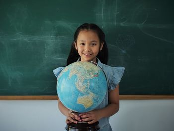 Portrait of smiling girl holding globe while standing in classroom