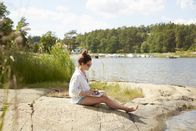 Woman using laptop at lake barefoot