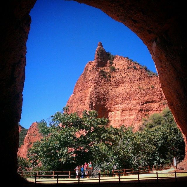 clear sky, tree, blue, built structure, low angle view, rock formation, architecture, sunlight, tranquility, mountain, nature, copy space, rock - object, day, indoors, beauty in nature, sky, travel destinations, tranquil scene, shadow