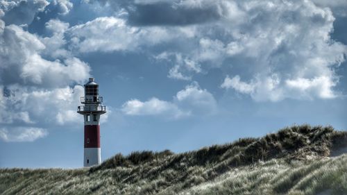 Lighthouse on field by building against sky