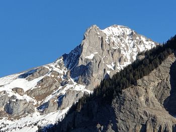 Low angle view of snowcapped mountains against clear blue sky