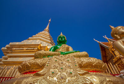 Low angle view of buddha statue by temple against clear blue sky during sunny day