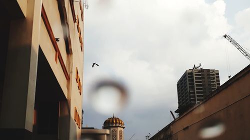 Buildings seen through car windshield against cloudy sky