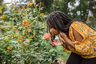 Side view of girl smelling flower while standing in park