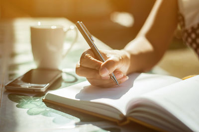 Midsection of woman writing in book at table