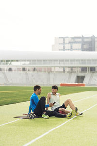 Male athletes sitting on grass against sky